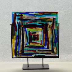 an abstract painting is displayed on a black stand with a white wall in the background