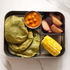 a metal container filled with food on top of a white table next to a bowl of fruit