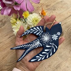 a hand holding a blue bird ornament with flowers in the background