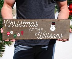 a man holding a wooden sign that says christmas at the wilsons