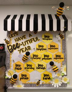 a bee themed bulletin board with bees and flowers on the front, hanging from a black and white striped awning