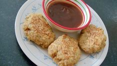 three fried food items on a plate next to a cup of dipping sauce and spoon