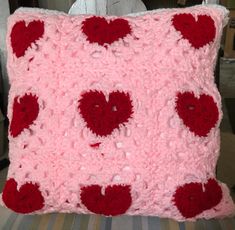 a crocheted pillow with red and pink hearts on the front is sitting on a chair