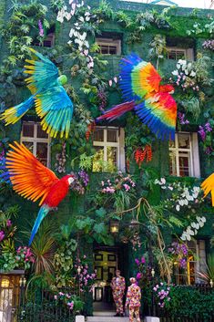 colorful parrots are painted on the side of a building with flowers and greenery