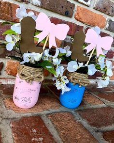 two mason jars with flowers in them are sitting on a brick wall next to a blue and pink vase