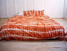 an orange and white comforter on a bed in a room with wood flooring