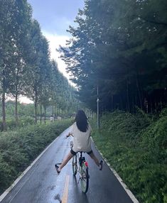 a person riding a bike down the middle of a road in front of some trees