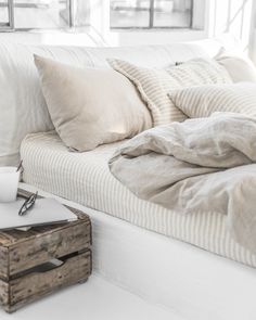 an unmade bed with white sheets and pillows on it, next to a window