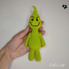 a hand holding a small green crocheted toy with a smile on it's face