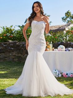 a woman in a wedding dress standing on the grass with her hand up to her chest