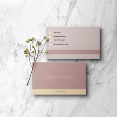 two pink business cards with gold foil lettering on them and a plant in the middle