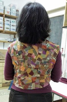 a woman standing in front of a counter wearing a colorful vest over her shoulder and black pants