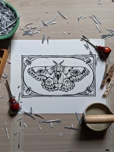 a drawing of a moth on paper next to some scissors and other crafting supplies