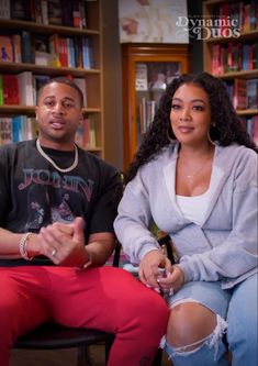 a man and woman sitting next to each other in front of a bookshelf