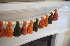 an orange and green tasselled garland hanging from a fireplace mantel