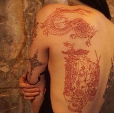 the back of a woman's body with dragon tattoos on her left shoulder and right arm