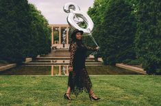 a woman in a black dress is holding a large silver balloon shaped like the number six