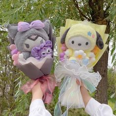 two stuffed animals are being held by someone's hands in front of a tree