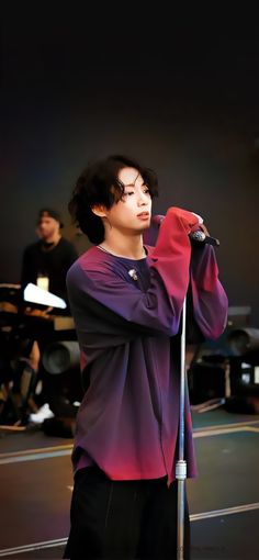 a young man holding a microphone while standing on top of a stage with other people in the background