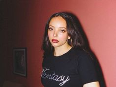 a woman standing in front of a red wall wearing a black shirt with the word friday written on it