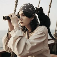 a woman with a black cat on her shoulder looking through binoculars at the ocean from a ship