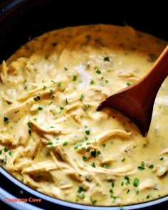 a wooden spoon in a crock pot filled with chicken and cheese