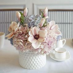 a white vase filled with lots of pink and purple flowers on top of a table