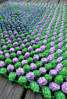 a crocheted blanket with purple and green flowers on it sitting on a wooden surface