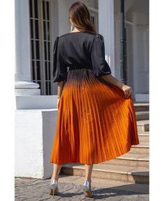 a woman in an orange pleated skirt is walking down the street with her back to the camera