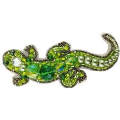 a brooch with green and white beads on it's back, in the shape of a lizard