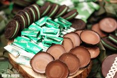 chocolates and cookies are arranged on top of a wooden slice with green wrappers