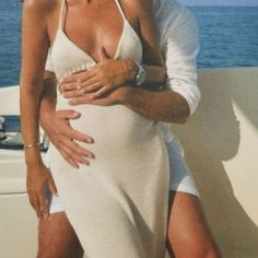 a woman in a white dress hugging a man on a boat with the ocean behind her