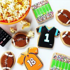 cookies decorated to look like footballs and shirts with sprinkles next to a bowl of popcorn