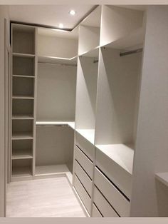 an empty walk in closet with white shelves and drawers on both sides, along with no doors