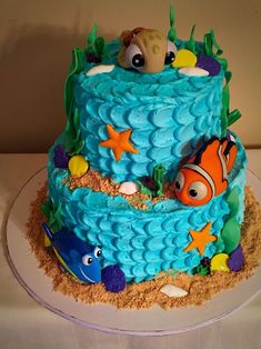 a birthday cake with an ocean theme and fish on the bottom tier is decorated in blue icing