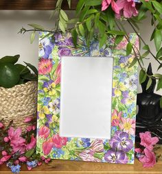 a flowered photo frame sitting on top of a wooden table next to potted plants