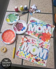 paper plates with mom's artwork on them next to paintbrushes and paints