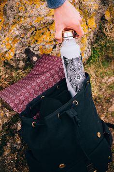 a person is holding a water bottle in their hand while standing next to a bag