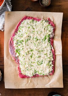 raw meat with parmesan cheese on top sitting on a piece of parchment paper