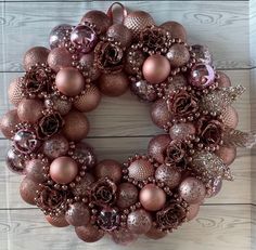 a christmas wreath with pink and gold ornaments on it sitting on a wooden table next to a wall