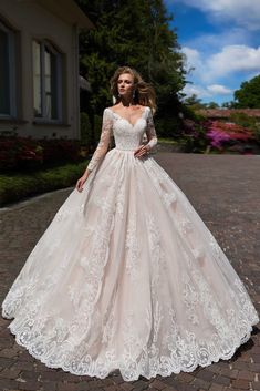 a woman in a wedding dress standing on a cobblestone road with her hands behind her back