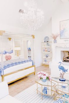 a white bedroom with blue and pink accessories on the bed, chandelier, fireplace, and couch