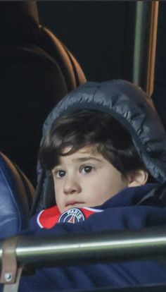 a young boy in a blue jacket sitting on a bench with his head turned to the side