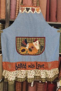 an apron that says baked with love hanging on a rack in a store filled with fabric