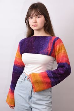 a young woman is posing for the camera wearing a colorful sweater and denim shorts with her hands on her hips