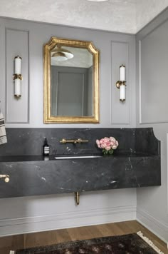 a bathroom with gray walls and gold trim on the mirror above the sink is a black marble countertop