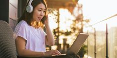 a woman with headphones on is using her laptop and listening to music while sitting outside