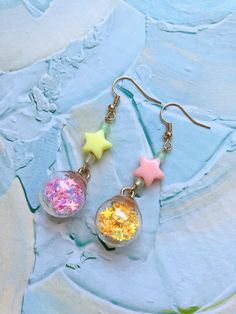 dd a touch of the night sky to your look with these enchanting star-themed dangle earrings. Each earring features a sparkling dome filled with tiny, twinkling stars, capturing the magic of a starlit night. Choose from two mesmerizing color pairs: ⭐︎Blue and Purple, reminiscent of a serene twilight sky, ⭐︎Yellow and Pink, evoking the glow of stars in a clear night sky. These lightweight plastic earrings are perfect for anyone who loves to carry a piece of the cosmos wherever they go. Whether you're dressing up for a special occasion or adding a bit of sparkle to your everyday outfit, these earrings are sure to catch the eye and brighten your day. Celestial Star-shaped Sparkling Earrings, Sparkling Star-shaped Celestial Earrings, Dangle Earrings With Star Charm For Party, Party Drop Earrings With Star Charm, Whimsical Star-shaped Jewelry With Star Charm, Trendy Star-embellished Jewelry Gift, Trendy Star Embellished Jewelry Gift, Trendy Star Embellished Jewelry For Gifts, Whimsical Star-shaped Party Jewelry