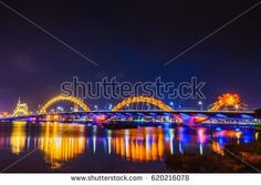 an illuminated bridge over the water at night with colorful lights and buildings in the background