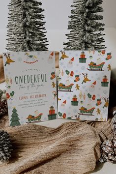 two christmas cards sitting on top of a table next to pine cones and fir trees